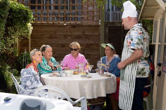31_07_coro_garden_party_03 Debbie, Bernie, Sally and Mary are served drinks by Tim, who is wearing a chefs hat, in a garden scene from Coronation Street