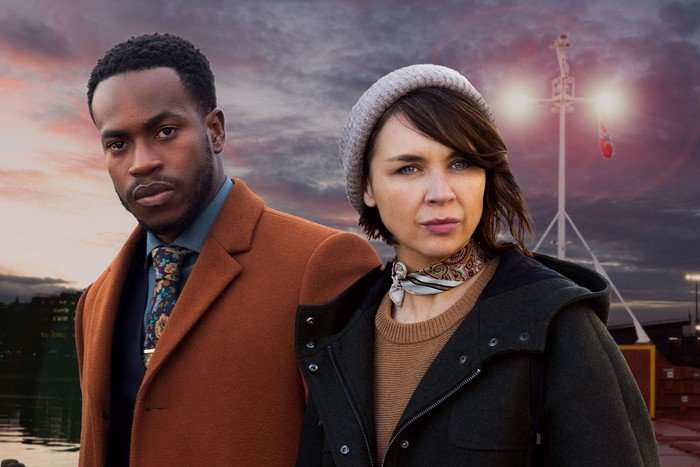 Granite Harbour Romario Simpson as Lindo and Hannah Donaldson as Bart in Granite Harbour, stood in front of the harbour