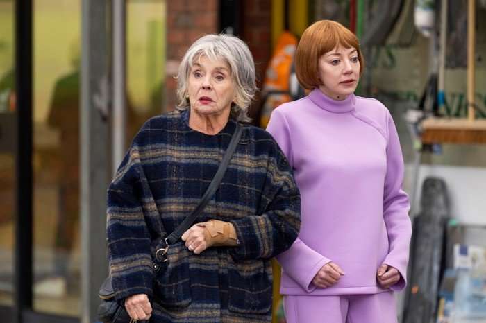 565478,TITLE:Ann Droid Sue and Ann Droid stand next to each other on a street. Sue looks shocked by something, while Ann is looking vacantly into the middle distance