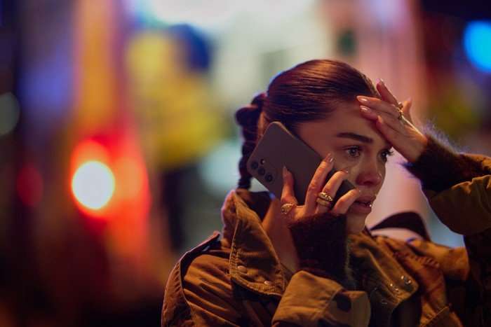 568993,TITLE:I, Jack Wright Sabrina Bartlett as Bella in I, Jack Wright, stood outside at night and speaking on the phone. She has her hand to her forehead and looks shocked and distressed.