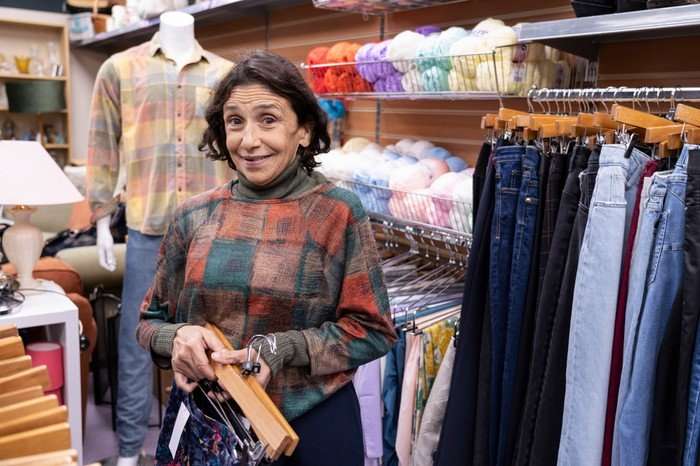 Kathryn Hunter as Eileen in Ann Droid, stood in a shop with clothes all around her on display.