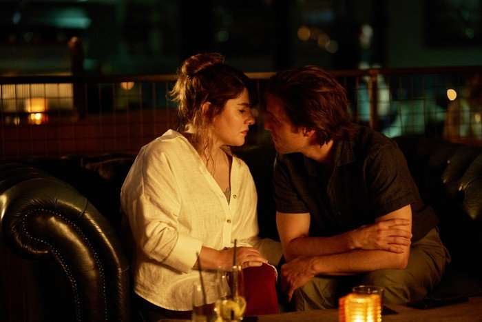 Ruth Madeley as Dr Gabriele Fox and Jack Farthing as Frasier Melville in The Rapture, sat together, leaning in to kiss.