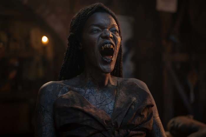 The Queen of the Damned bears her fangs as she stands in a dark, cavernous space