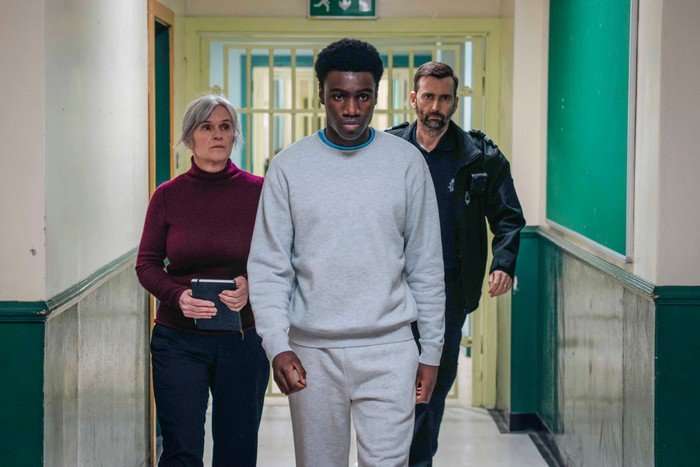 571859,TITLE:TIME - Series 3 Chukwubuikem Molokwu as Christopher in Time season 3, walking down a prison hallway with a staff member behind him on each side