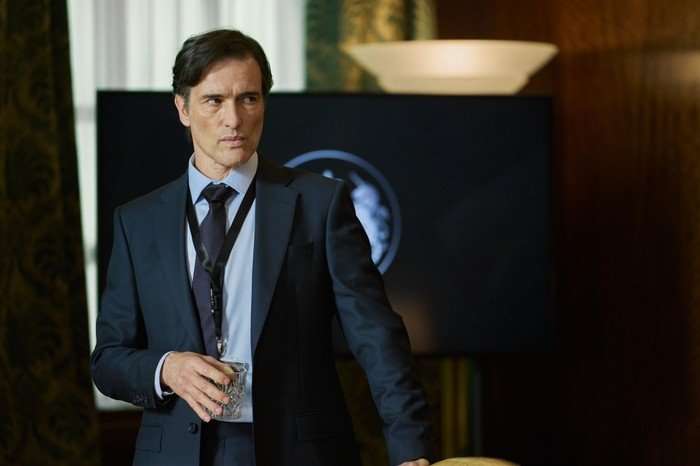 The Undeclared War - Series 2 Ep2 Ed Stoppard as Richard Marston in The Undeclared War, wearing a suit and stood in front of a TV screen.