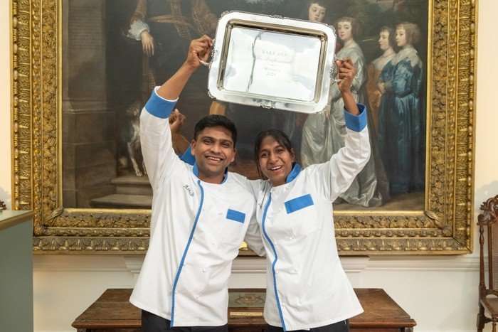 Bake Off: The Professionals S11 Ep11 Ashish and Loki stood next to each other holding a trophy above them and smiling ahead.