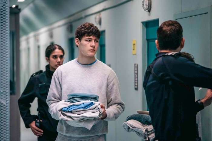 571860,TITLE:TIME - Series 3 Ollie McNulty plays Peter Palmerston in Time season 3; he is holding folded uniforms while standing outside his prison cell, talking with two prison staff members
