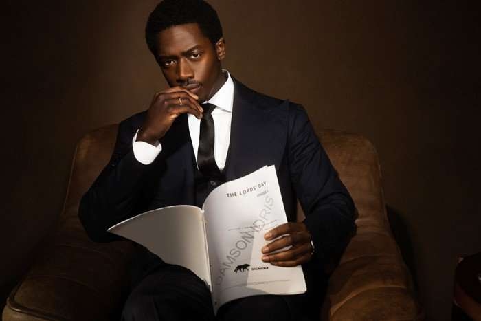 DAID_0185_V1 Damson Idris, wearing a suit and sat in an armchair, reading the script for The Lords' Day.