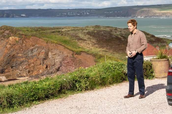 Bergerac S1 Damien Molony as Jim Bergerac standing in front of a coastal backdrop