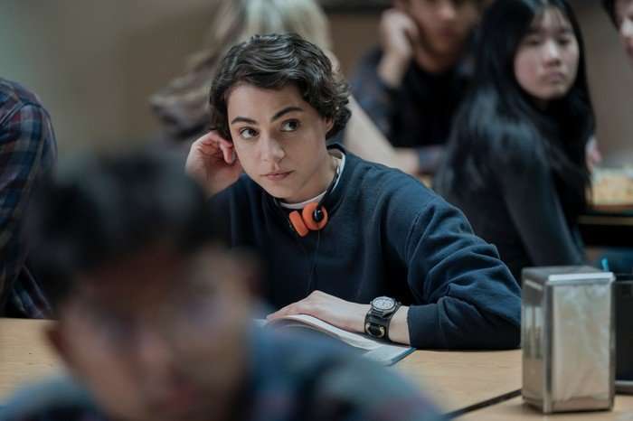 Gabrielle Policano as Liz in Elle, sat at a desk with headphones around her neck.