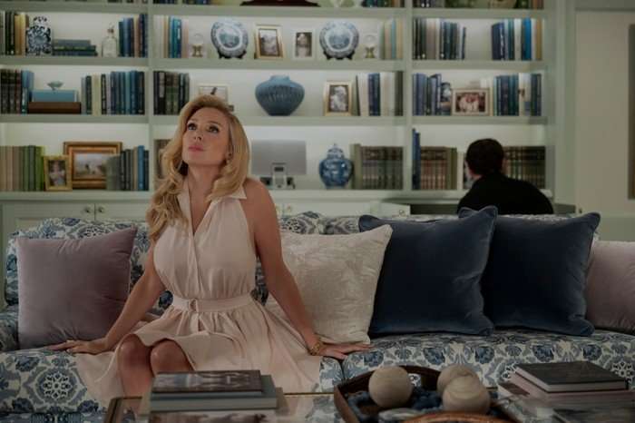 June Diane Raphael as Eva Woods in Elle, wearing a white dress and sat in a living room.