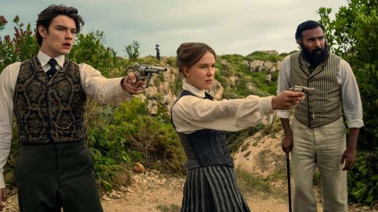 "Three people in vintage clothing stand outdoors in a rugged, green landscape; two point pistols ahead while the third stands beside them with a cane, all looking alert and tense." Enola Holmes 3. (L to R) Louis Partridge as Tewkesbury, Millie Bobby Brown as Enola Holmes and Himesh Patel as Dr. Watson in Enola Holmes 3. Cr. John Wilson/Netflix &copy;2026