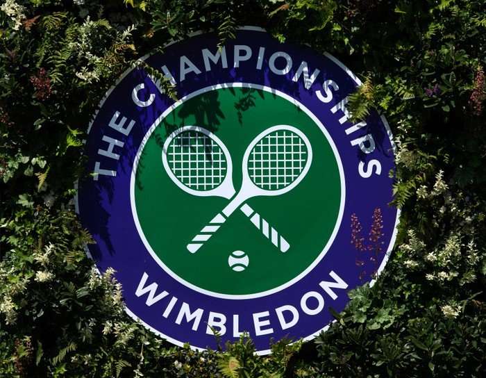 Wimbledon 2026 TV The green and purple Wimbledon logo, with white tennis rackets on it, with bushes around the outside.