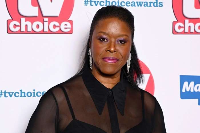 Michelle Greenidge, wearing a black top and stood in front of a white backdrop with the TV Choice logo on it.
