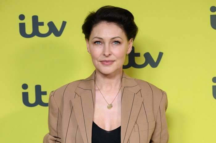 Emma Willis, wearing a brown jacket and a black top, stood in front of a yellow backdrop with the ITV logo on it.