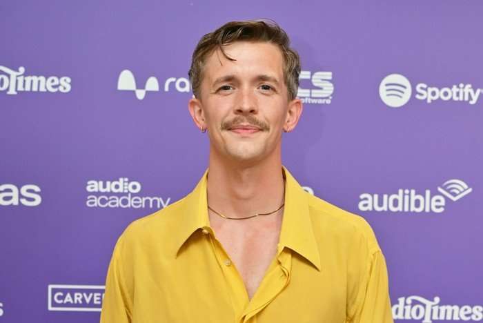 Stephen Libby stood wearing an unbuttoned yellow shirt with necklace smiling ahead.