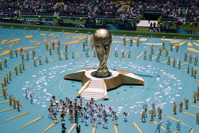 Performers on the pitch in front of a giant World Cup trophy.
