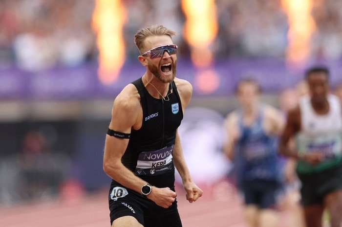 Scottish athlete Josh Kerr, in black running kit, celebrates on the track at the London Stadium.