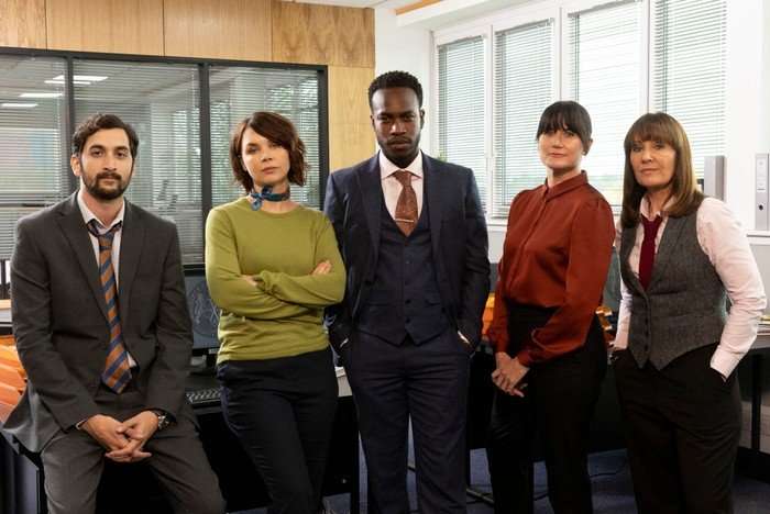 466897,Granite Harbour S2 Bhav Joshi as Jay Hannah Donaldson as Bart, Romario Simpson as Lindo, Dawn Steele as Cora, Michelle Jeram as Monty in Granite Harbour standing in the middle of a police station around a desk.