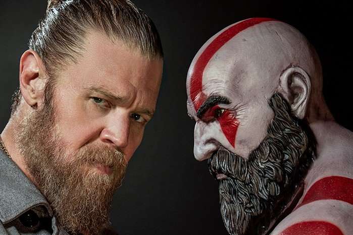 Kratos-actor-God-of-War A promo photograph of Ryan Hurst stood next to a statue of Kratos from God of War. Hurst, his hair tied back, stares down the lens. Kratos, meanwhile, stares right at Hurst.