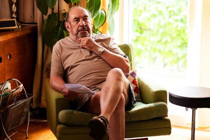 Austin Roy Billing as Bill, sat in a chair, legs crossed