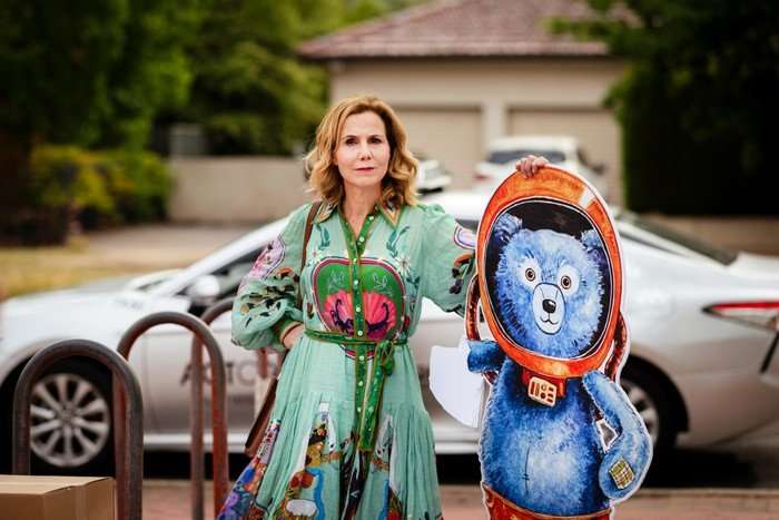 Austin Sally Phillips as Ingrid, standing in the street with a cardboard cut out of a big blue bear