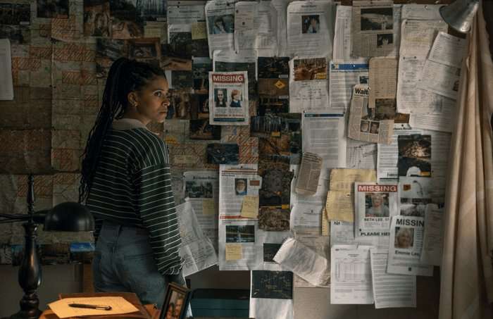 Zazie Beetz stands in front of a wall plastered with missing posters and newspaper clippings.