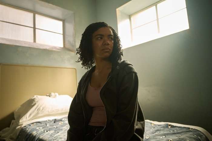 570504,TITLE:The Rapture India Amarteifio as Bethany Krall in The Rapture, sitting in her dorm room and on her bed as light streams in from narrow windows.