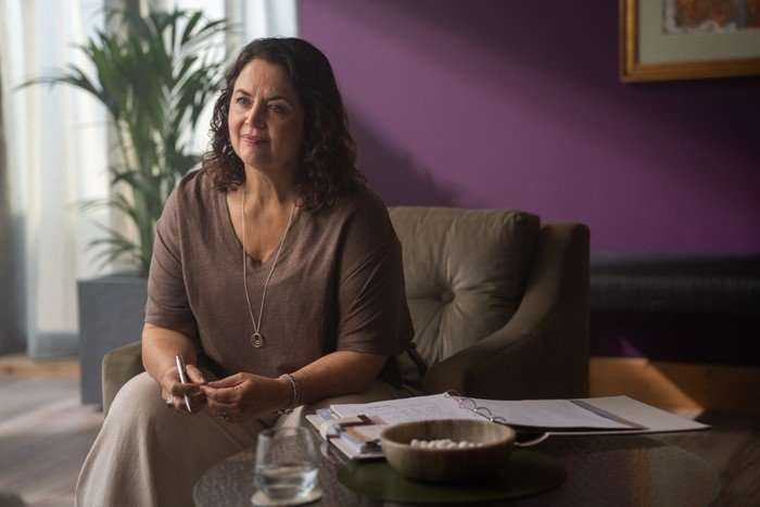 570514,TITLE:The Rapture Ruth Jones as Mel in The Rapture sitting in an armchair with a binder in front of her and holding a pen.