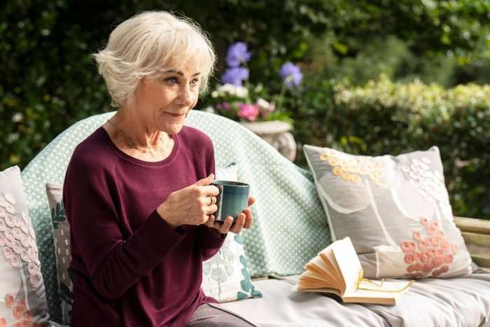 Zo&euml; Wanamaker as Charlie Hungerford, sat on a bench in a garden, drinking a cup of tea