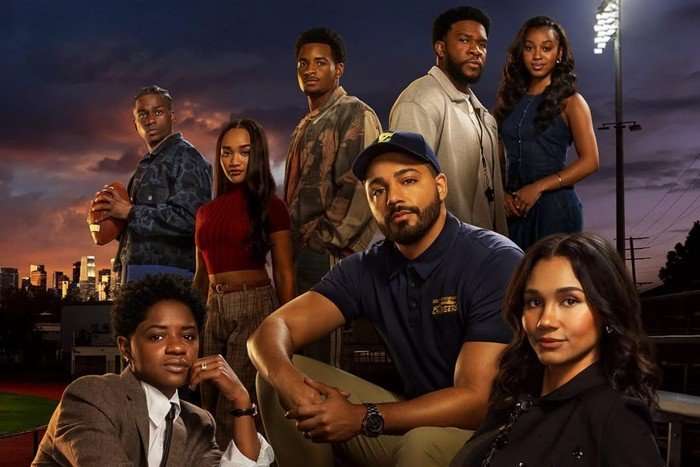 all-american-s8-cast The cast of All American sitting on a football field, posing.