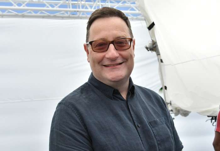 Chris Chibnall wearing sunglasses and a blue shirt standing outside and smiling at the camera.