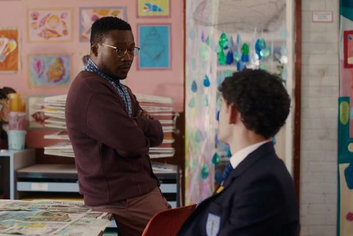 Mr Ajayi perches on a desk while speaking to Charlie about something in his classroom