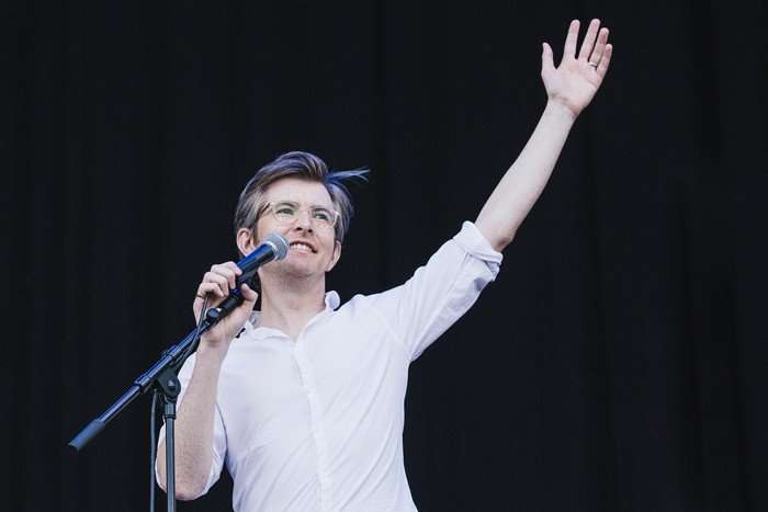 Latitude Festival 2015 - Day 4 Gareth Malone addresses a festival crowd with one arm raised, wearing glasses and a white shirt beside a microphone stand.