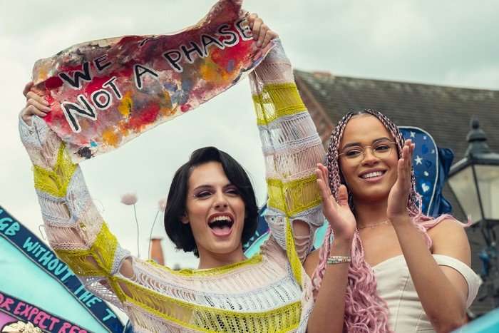 Naomi and Elle smile and dance on a Pride parade float calling for trans rights