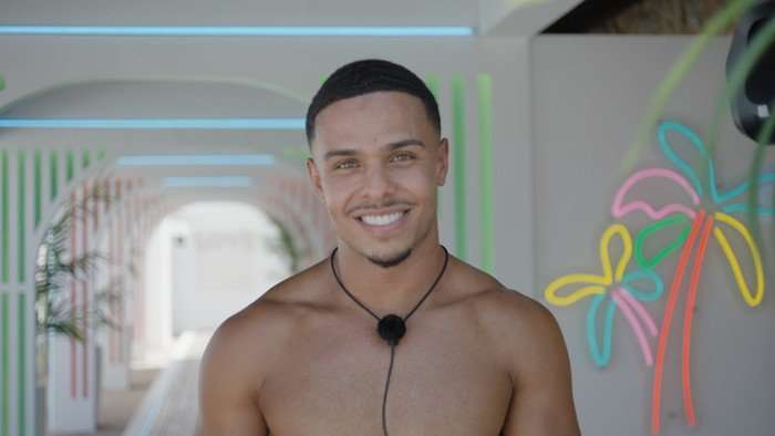 Love Island S13 A topless Ethan smiling ahead as he stands in the villa tunnel.
