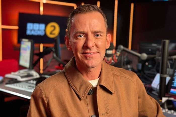 Scott Mills on BBC Radio 2 Scott Mills in the BBC Radio 2 studio, wearing a brown jacket and smiling at the camera.