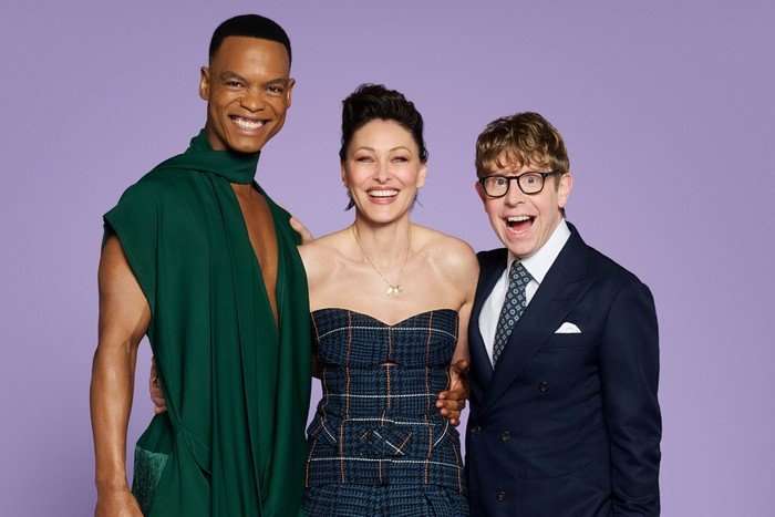 strictly-come-dancing (17) Johannes Radebe, Emma Willis and Josh Widdicombe stood in a row in front of a purple backdrop, all smiling ahead as they pose for a photo together.