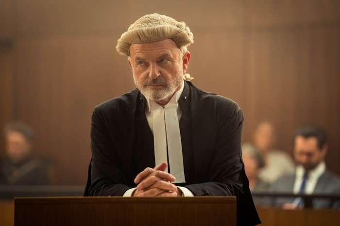 the_twelve_sam_neill Sam Neill as Colby SC resting his hands against a wooden stand, wearing a barrister gown and wig in The Twelve.