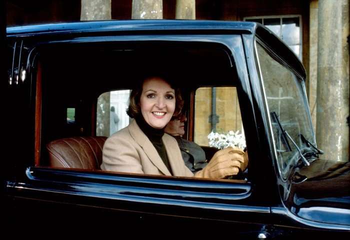 Penelope Keith as Audrey fforbes-Hamilton in To the Manor Born, sitting in a car, holding the steering wheel and smiling at the camera.