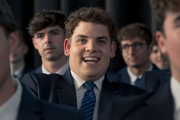 Isaac smiles while sat in a crowd of students at a school assembly