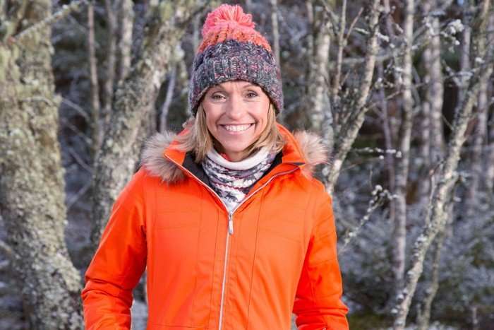 Michaela Strachan wearing a bright orange jacket and woolly hat, smiling ahead.